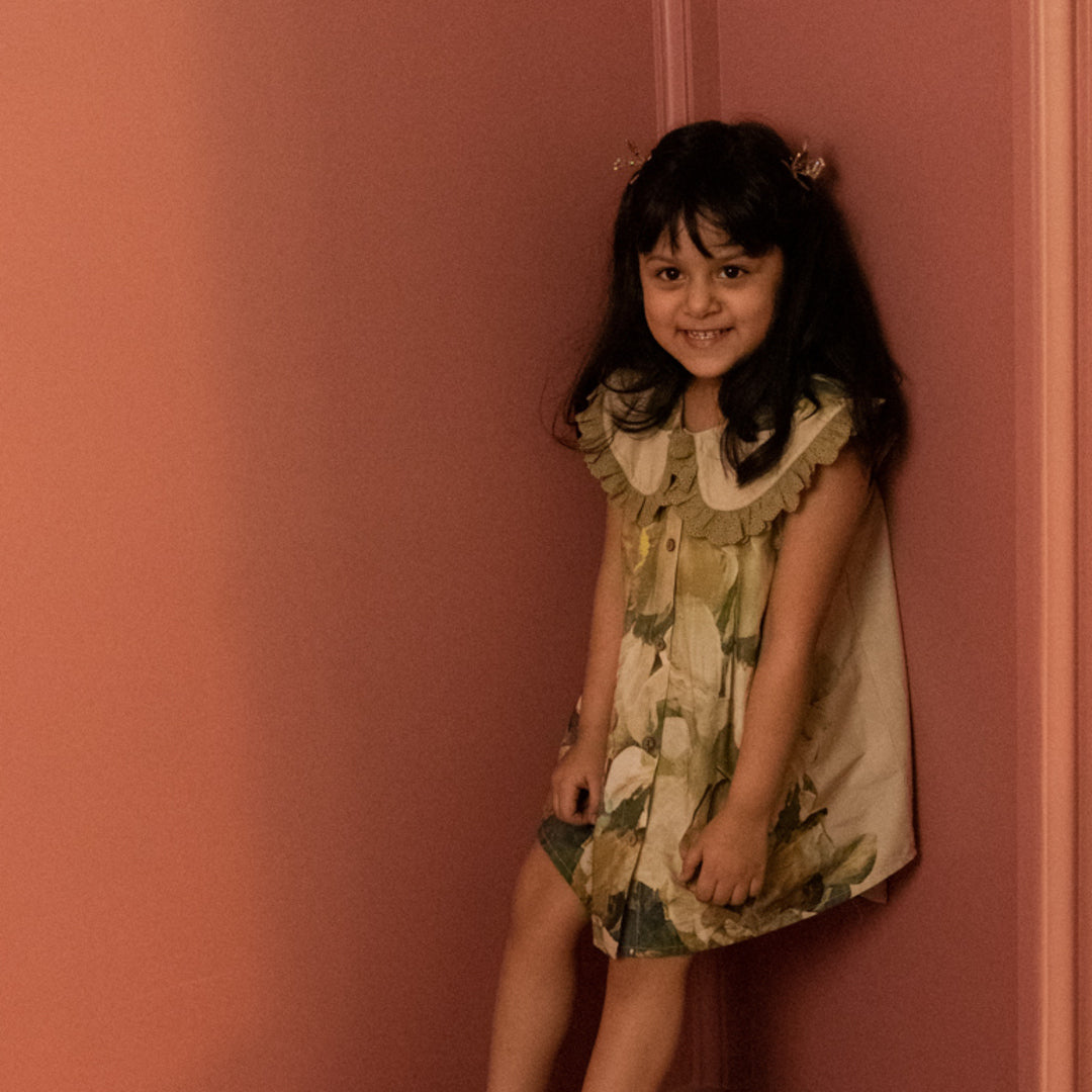 Young girl in a floral dress standing against a pink wall