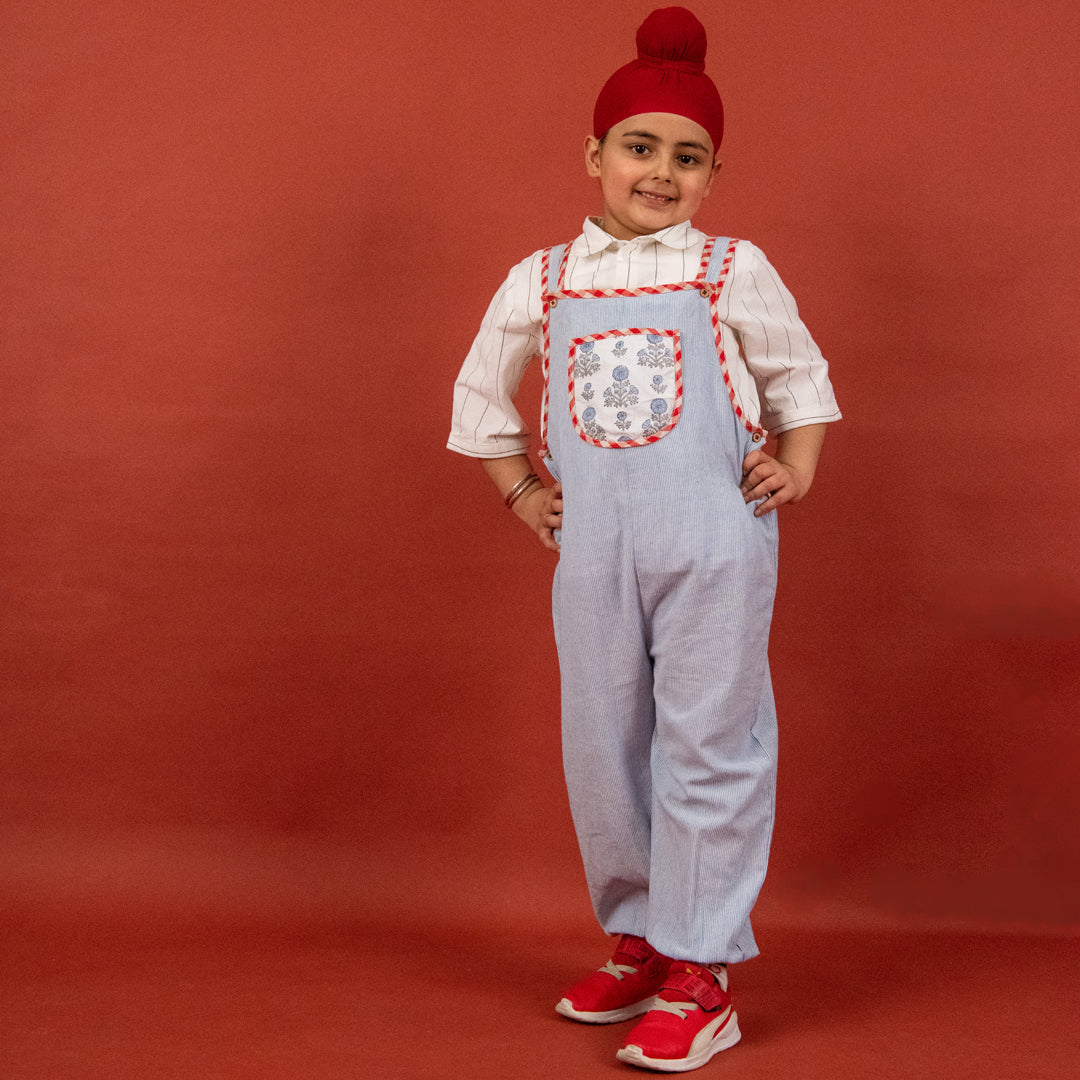 Child wearing a red hat, white shirt, and light blue overalls with a red background