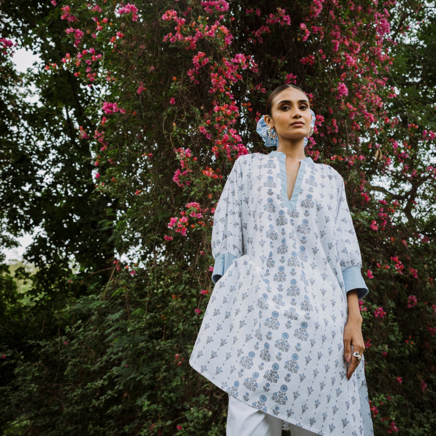 Woman wearing a light blue floral dress standing in front of a flowering tree