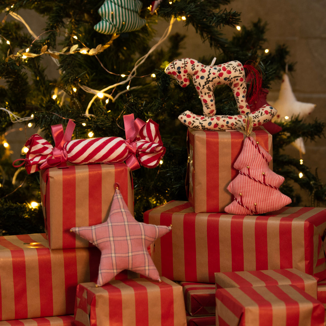 Stack of red and gold striped presents with decorative stars and ribbons against a Christmas tree background.