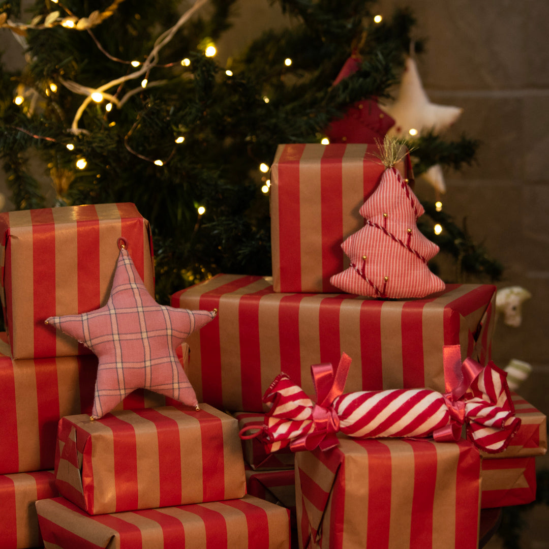Stack of red and brown striped Christmas presents with decorative stars and ribbons in front of a decorated tree.