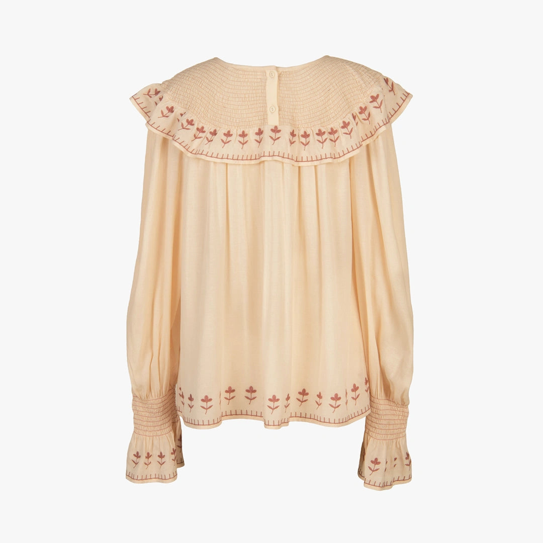 A light beige long-sleeve blouse with a wide pleated ruffled collar and matching ruffled cuffs, featuring delicate red floral embroidery along the edges.