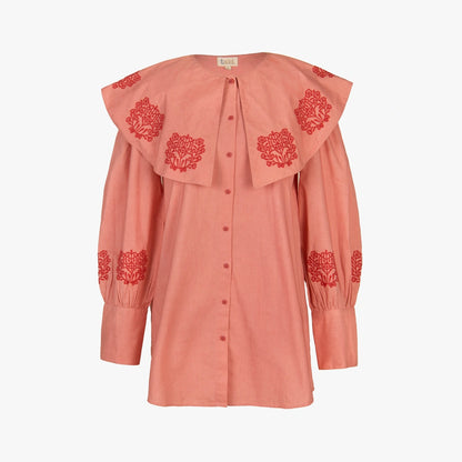 A dusty pink long-sleeve blouse with a large layered ruffled collar and red embroidered floral motifs, shown against a plain white background.