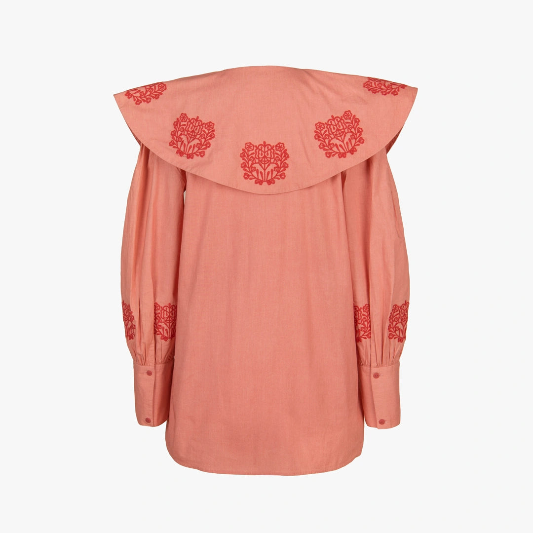 A peach-colored long-sleeve blouse with a dramatic oversized collar featuring red floral embroidery, and matching red embroidery on the cuffs, shown against a plain white background.