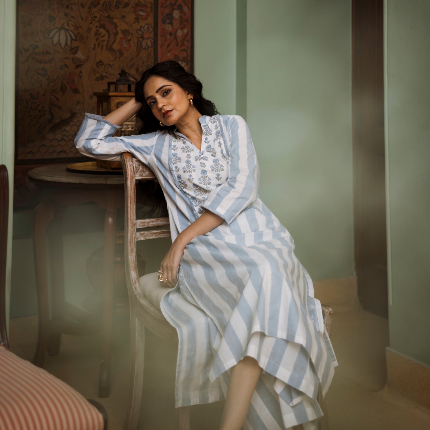 Woman in a blue and white striped dress sitting on a chair in a room with a textured wall.