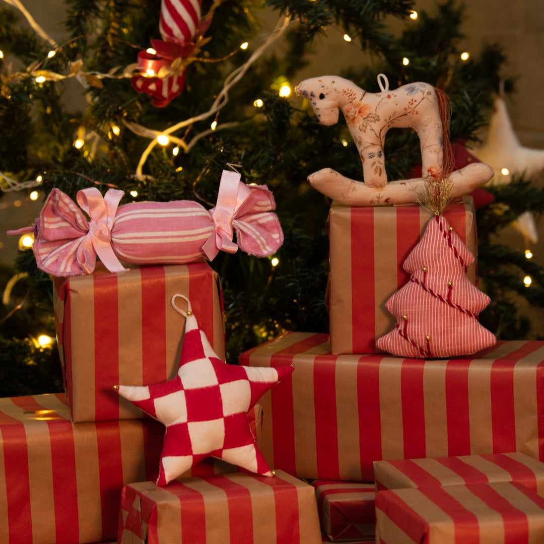 Stack of red and gold striped presents with decorative items against a Christmas tree background
