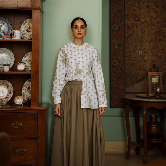 Woman in a floral blouse and brown skirt standing in a room with wooden furniture and decorative plates.