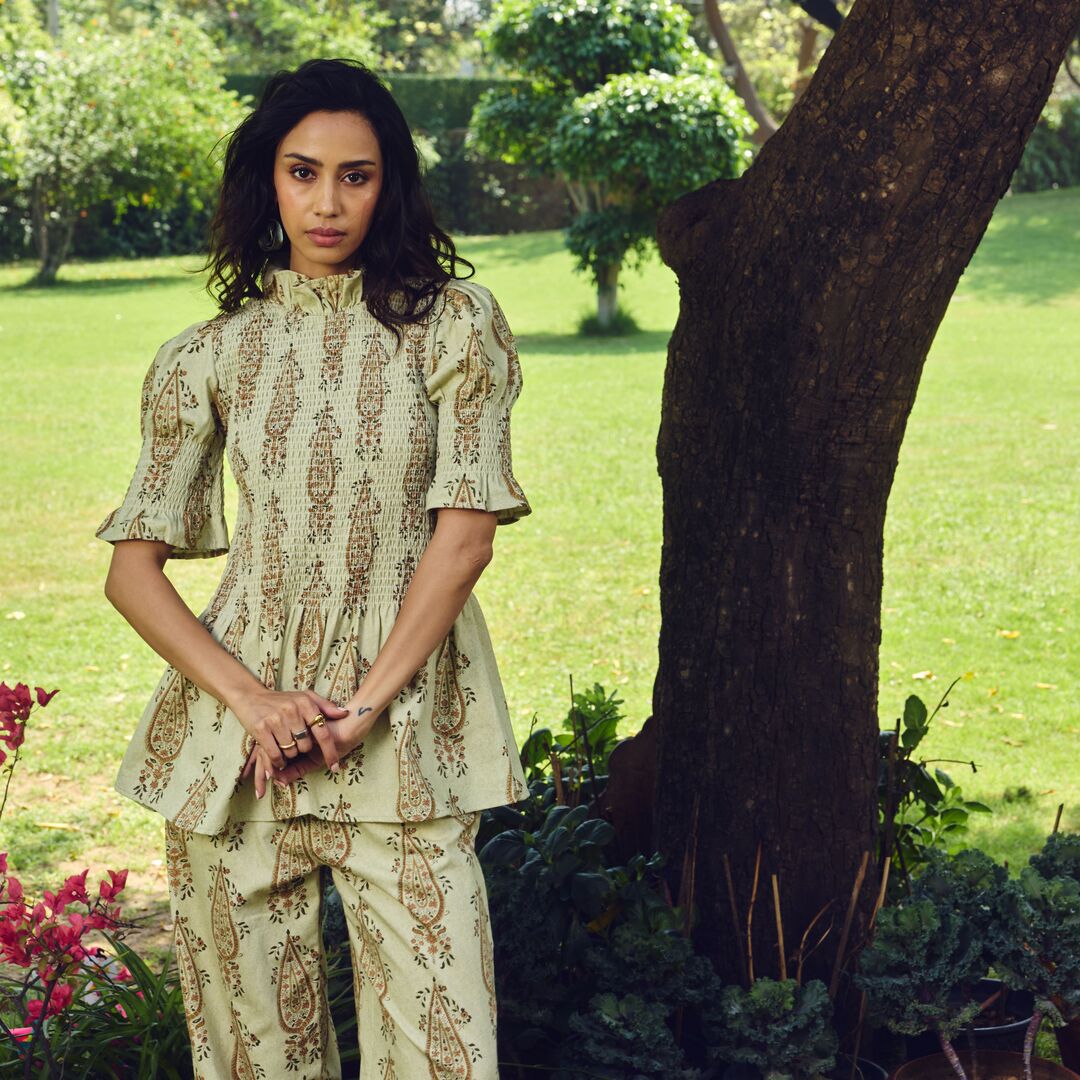 Woman in a patterned outfit standing in a garden with trees and grass.