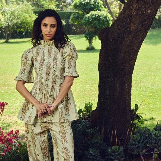 Woman in a patterned outfit standing in a garden with trees and grass.