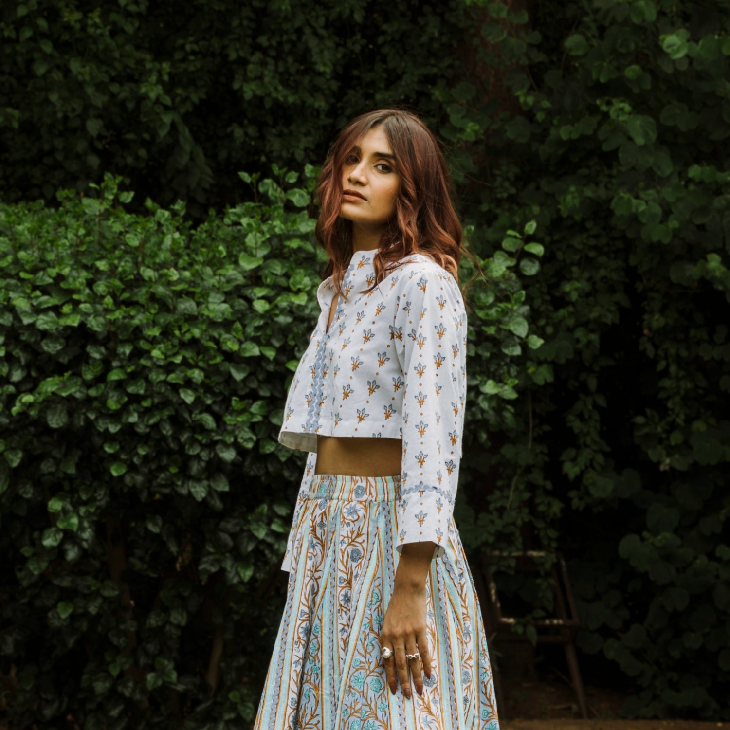 Woman in a patterned outfit standing against a green leafy background