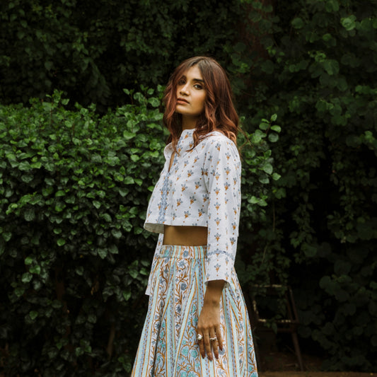 Woman in a patterned outfit standing against a green leafy background