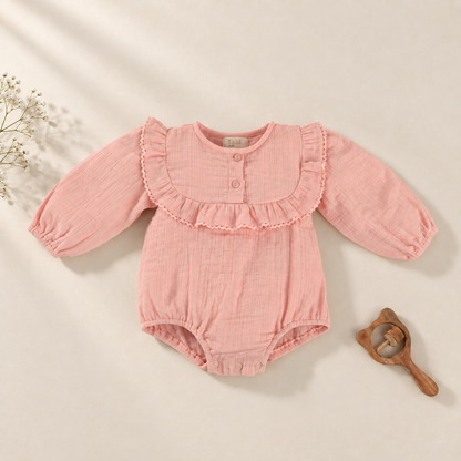 A baby long-sleeve romper in textured pink muslin fabric, featuring a ruffled collar with two front buttons and elasticized cuffs and leg openings. 