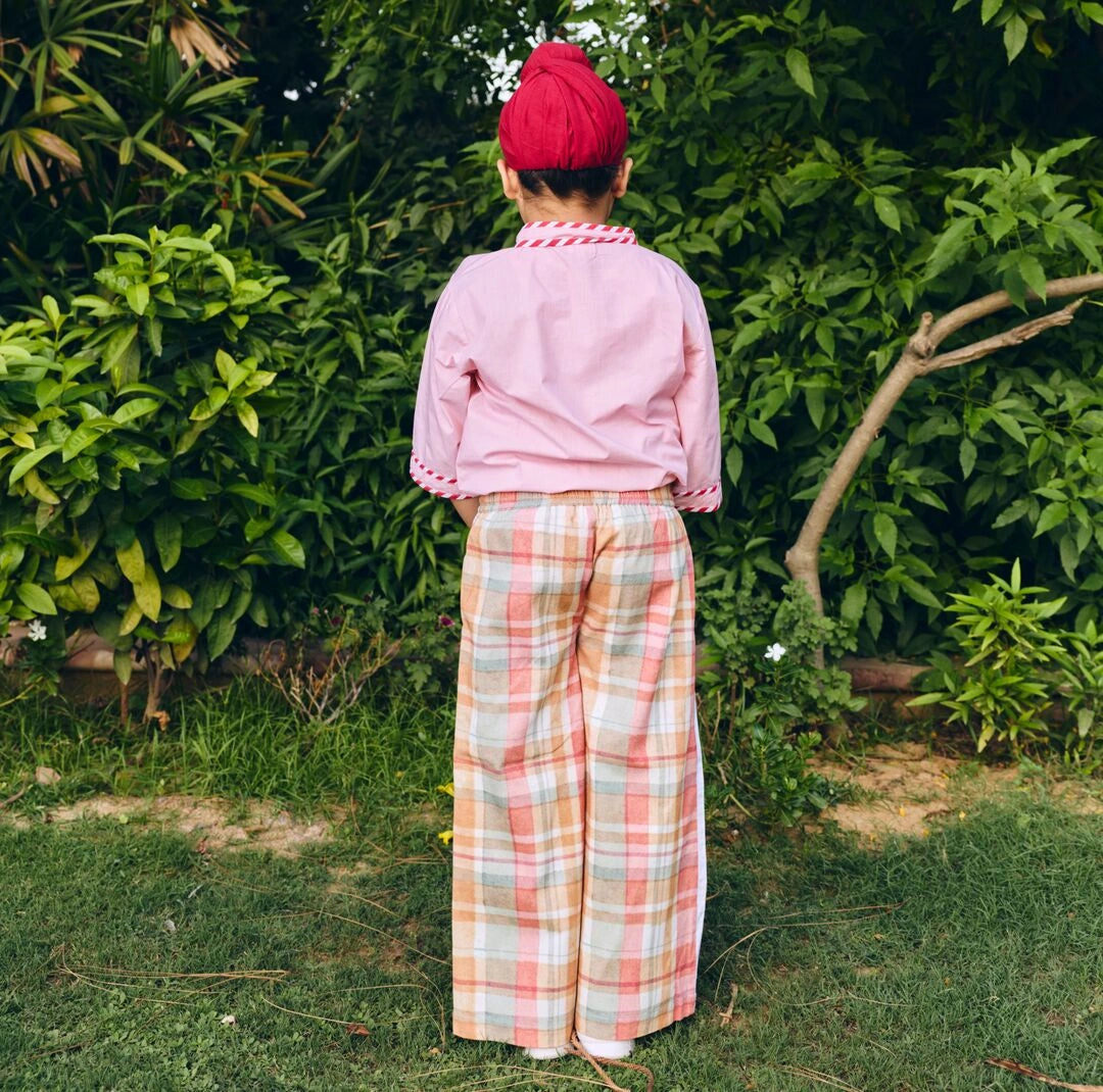  A child is wearing a light pink sleeve shirt with wide-leg plaid trousers in pink, beige check.