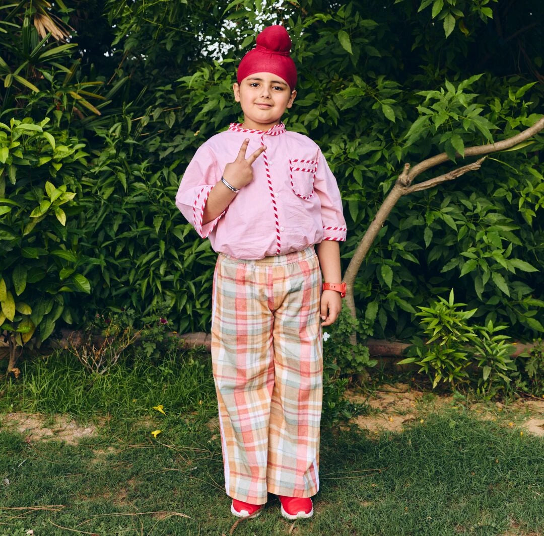 A young boy  wearing a pink short-sleeve shirt with  plaid trousers.