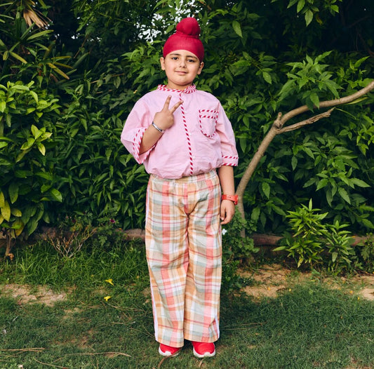A young boy  wearing a pink short-sleeve shirt with  plaid trousers.