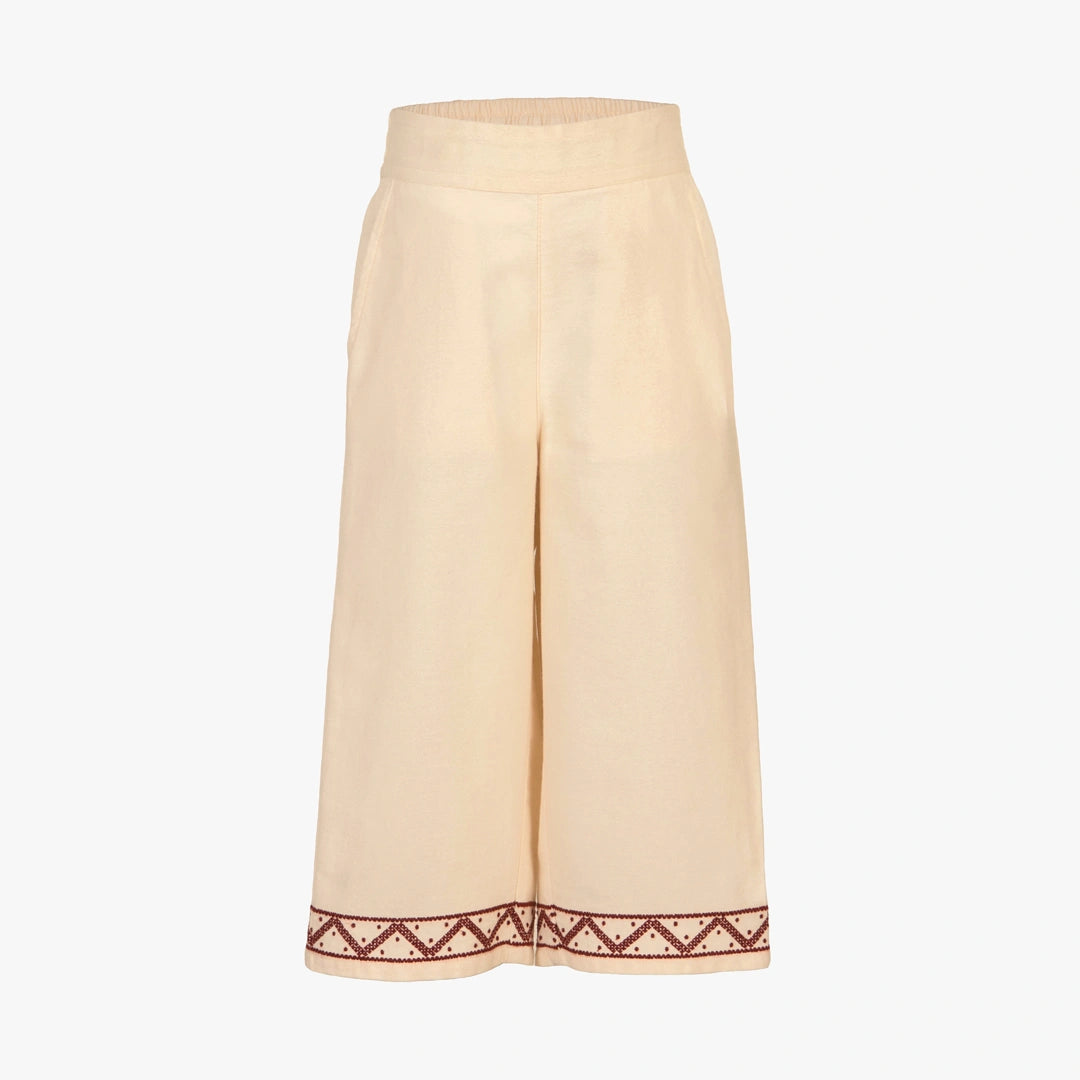 A pair of wide-leg cropped pants in a light cream or beige linen-like fabric, featuring a decorative embroidered border in dark red and white along the hem.