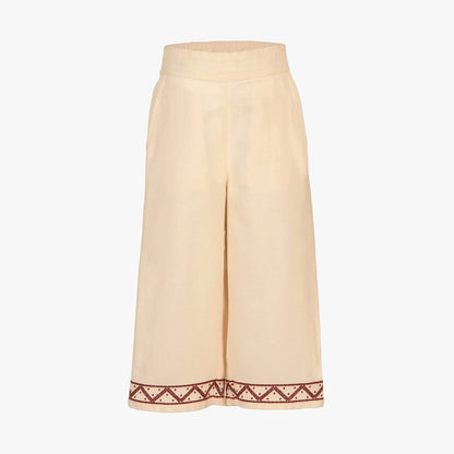A pair of wide-leg cropped pants in a light cream or beige linen-like fabric, featuring a decorative embroidered border in dark red and white along the hem.