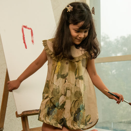 Young girl in a floral dress painting on an easel with a brush.