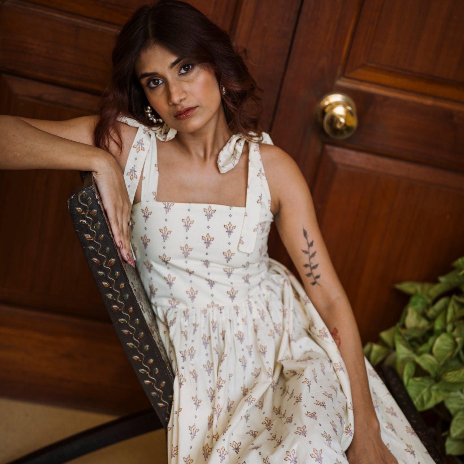 Woman in a white floral dress sitting against a wooden door.