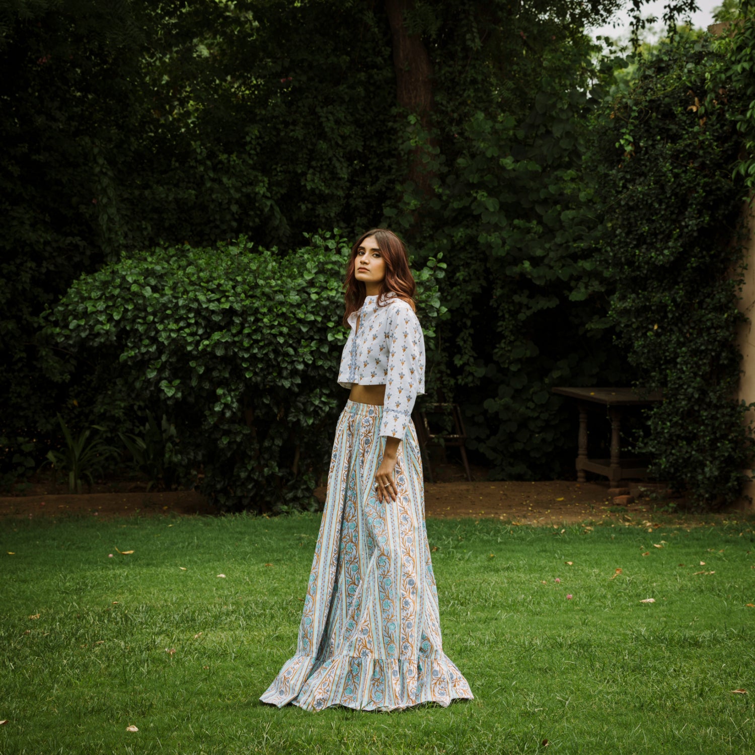 Woman in a patterned outfit standing in a garden with greenery