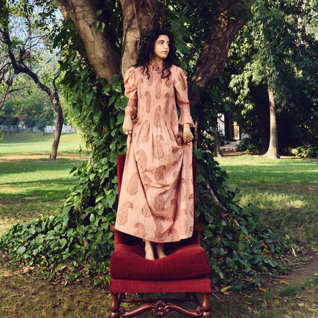 Woman in a patterned dress sitting on a red chair under a tree in a park.