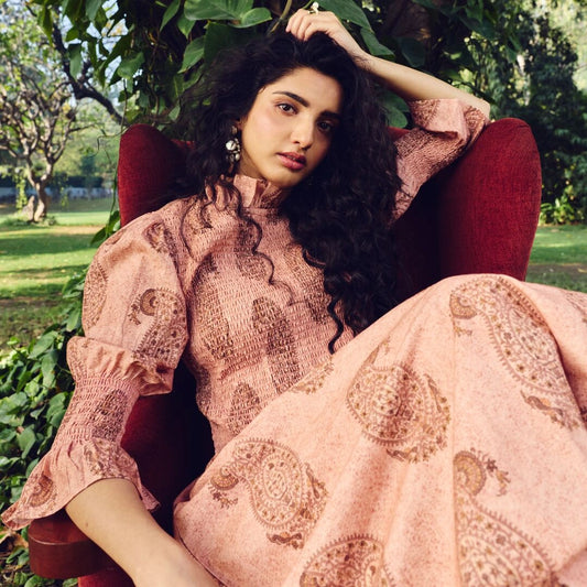 Woman in a pink patterned outfit sitting outdoors with greenery in the background