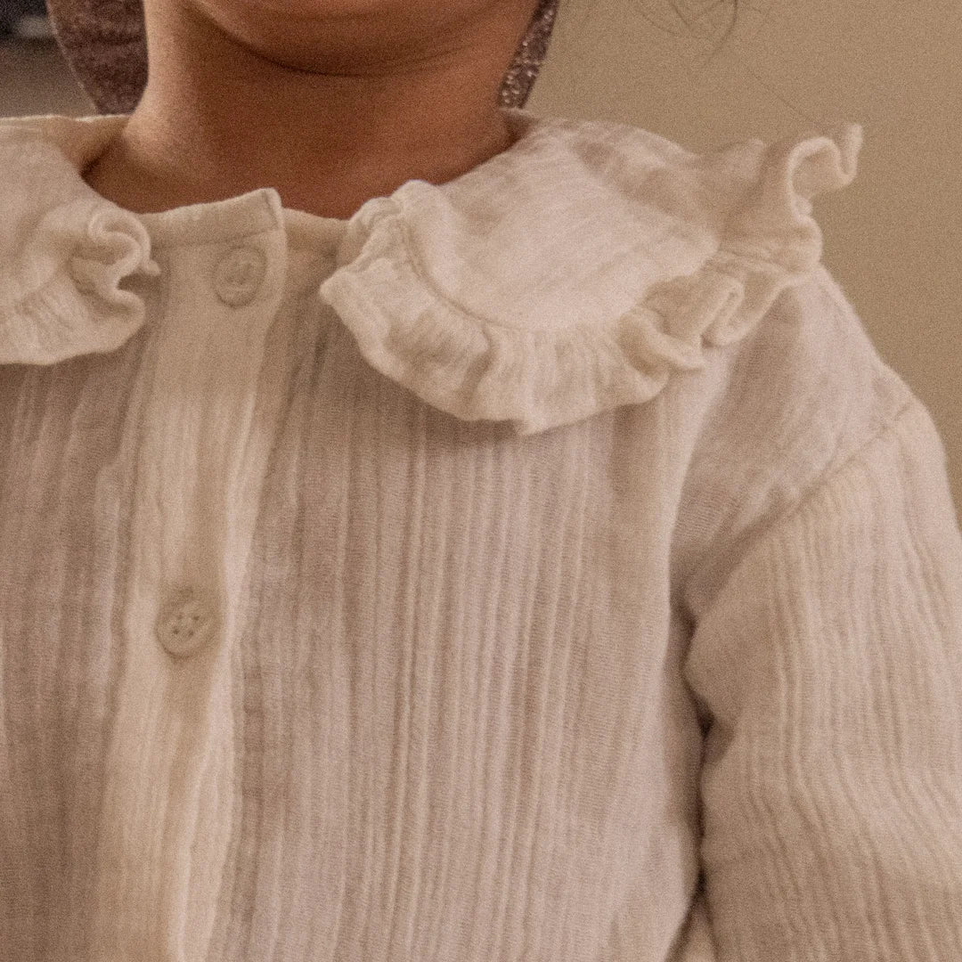 Close-up of a child wearing a cream-colored crinkle gauze top with a ruffled Peter Pan collar and front buttons.