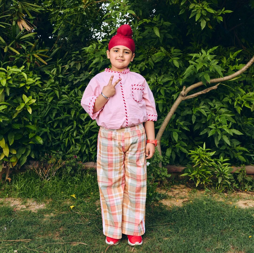 Child wearing a pink outfit with a red turban standing in a garden.