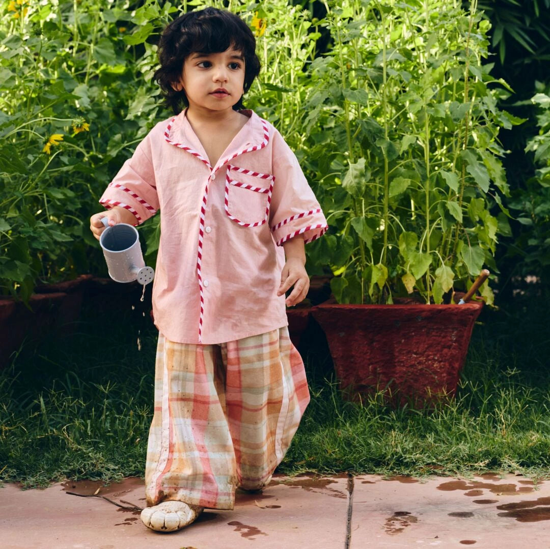 A young child wearing a light pink Check wide leg pants with white striped piping.