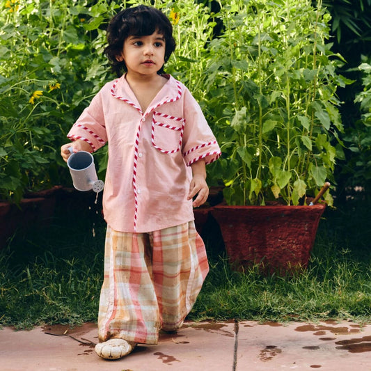 A young child wearing a light pink Check wide leg pants with white striped piping.