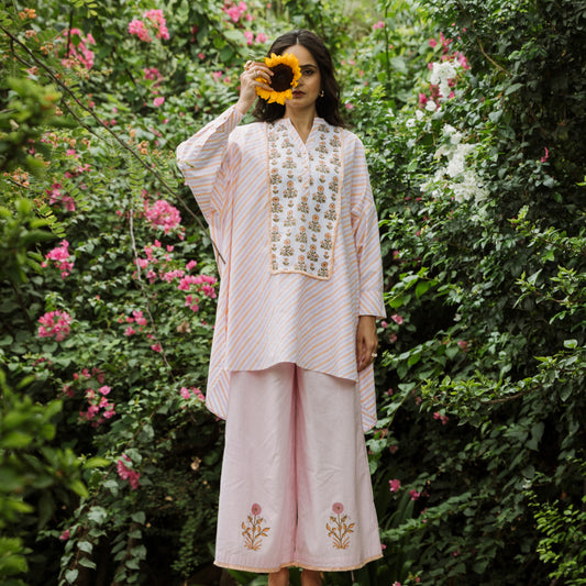 Woman in a light pink traditional outfit with floral embroidery standing in a garden.