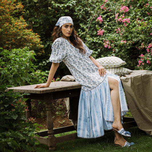 Woman in a patterned dress sitting on a wooden bench in a garden.