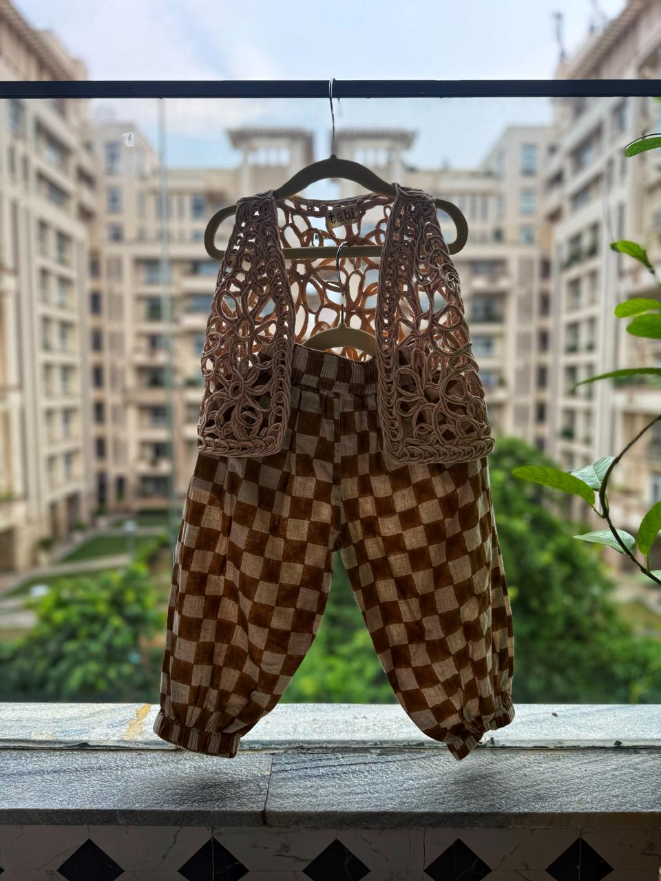 Brown crochet top and checkered pants on a hanger with a cityscape background