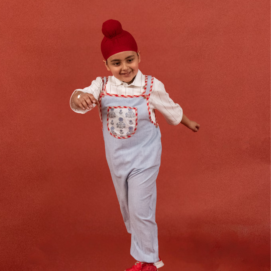 Child wearing a red hat and light blue overalls with a white shirt on a red background