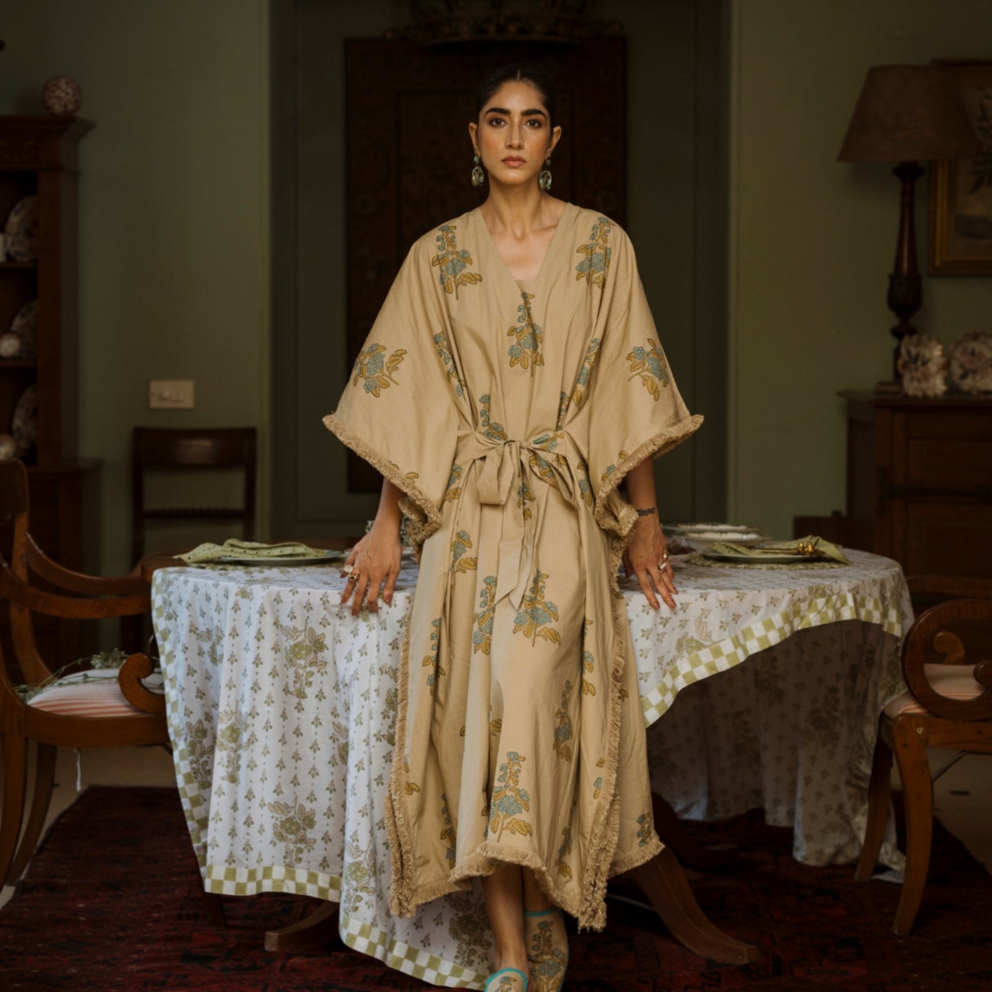 Woman in a floral dress standing in a room with a table and chairs.