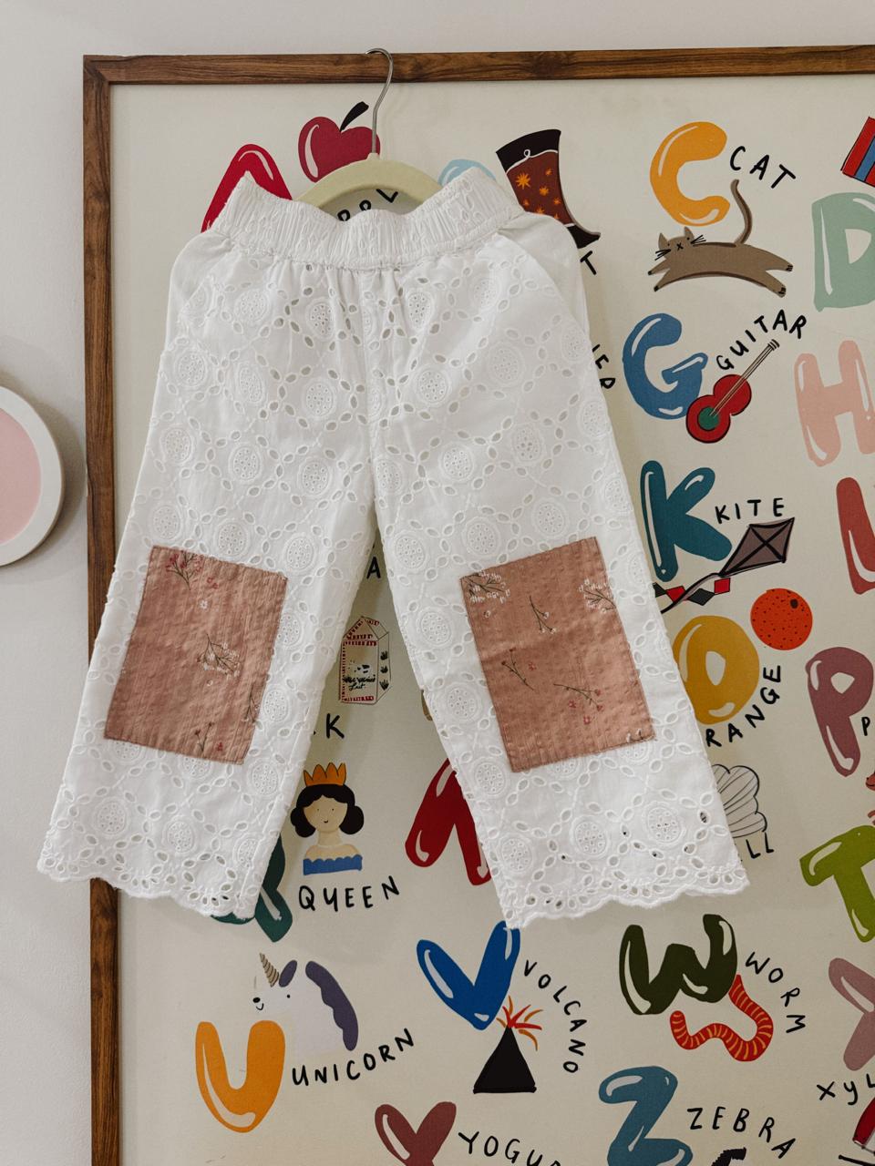 White lace pants with brown patches hanging on a colorful alphabet poster.