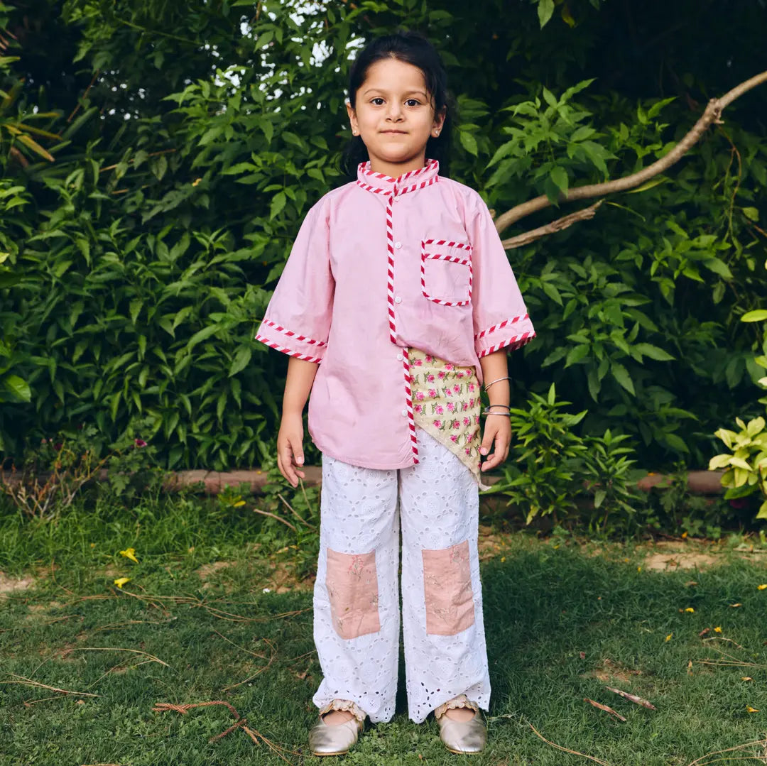 A young girl  wearing a pink patchwork-style short-sleeve top paired with white patchwork pants.