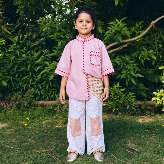A young girl  wearing a pink patchwork-style short-sleeve top paired with white patchwork pants.
