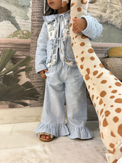 Child in light blue outfit holding a giraffe plush toy outdoors