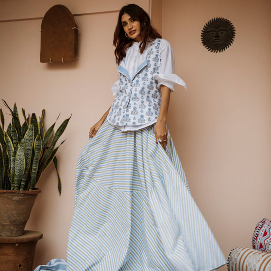 Woman in a floral top and striped skirt standing in a room with a plant and wall decorations.