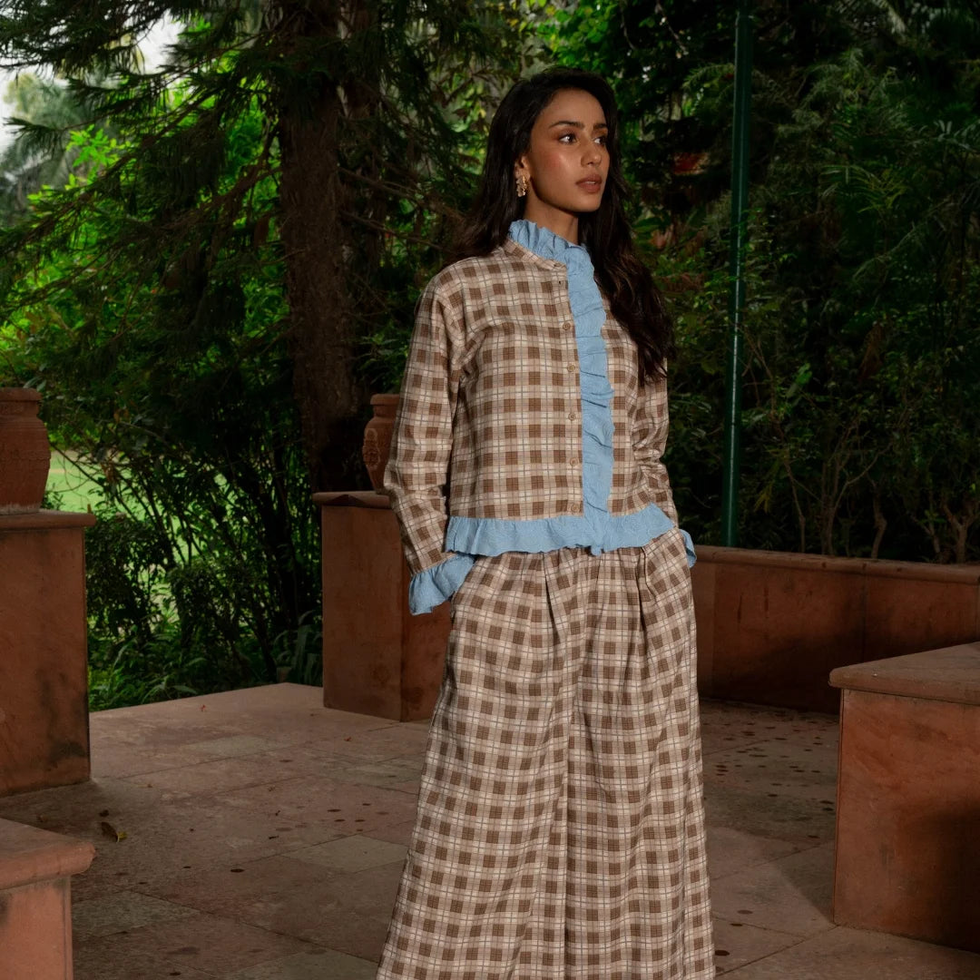 A woman stands wearing a matching two-piece outfit with a brown and beige plaid pattern and light blue ruffled trim details.