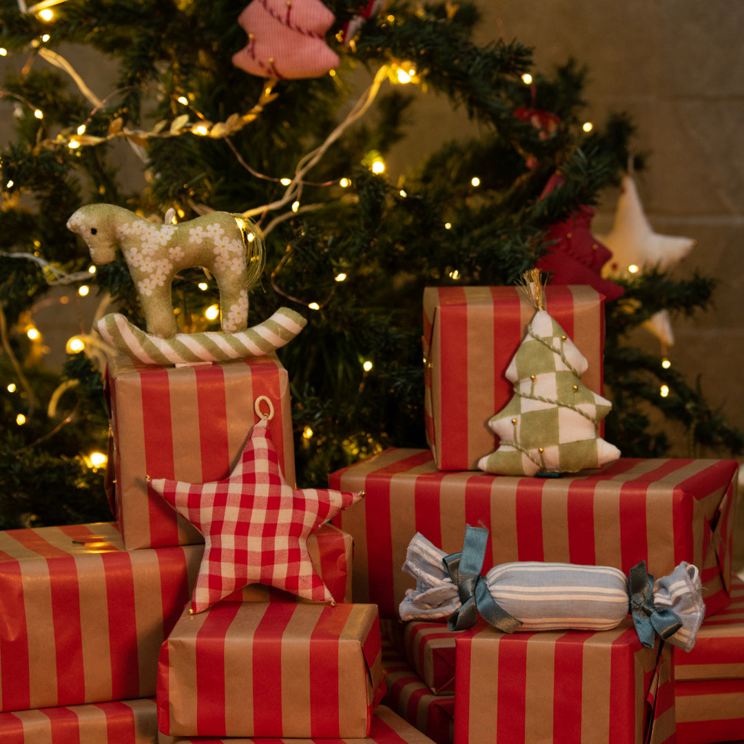 Stack of red and gold striped presents with decorative items against a Christmas tree background