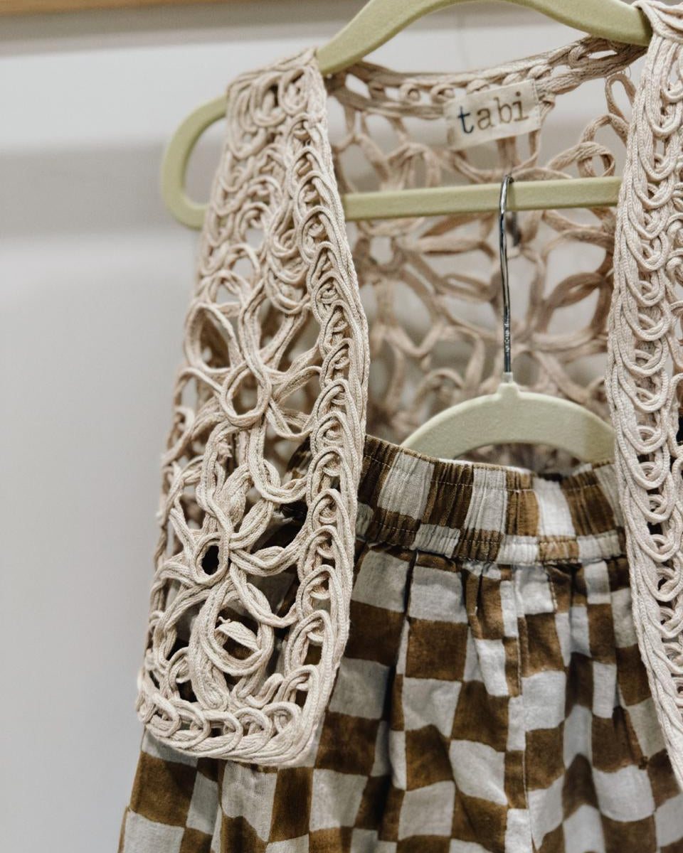 Brown and white checkered pants with a beige lace top on a hanger.