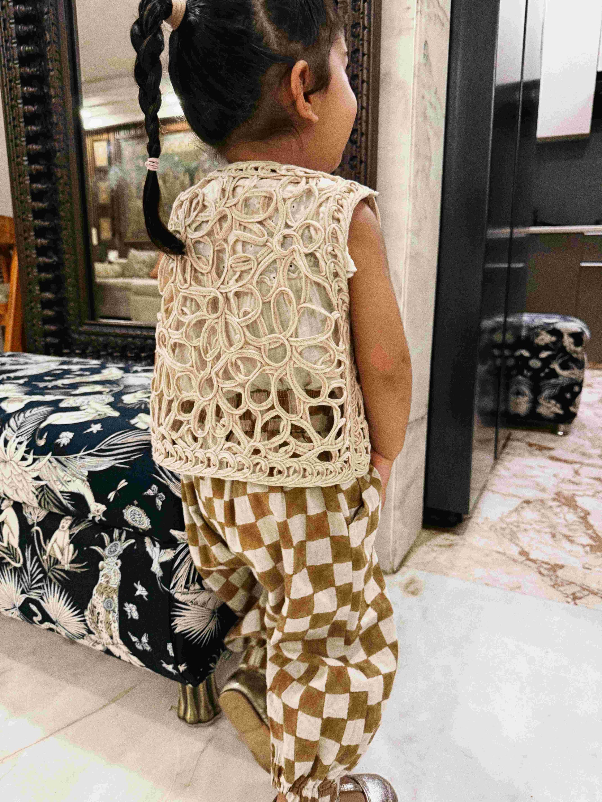 Child wearing a patterned outfit standing in a room with furniture.
