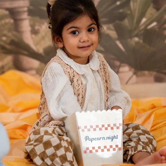 A young girl wearing  white top, a lace vest and checkered pants