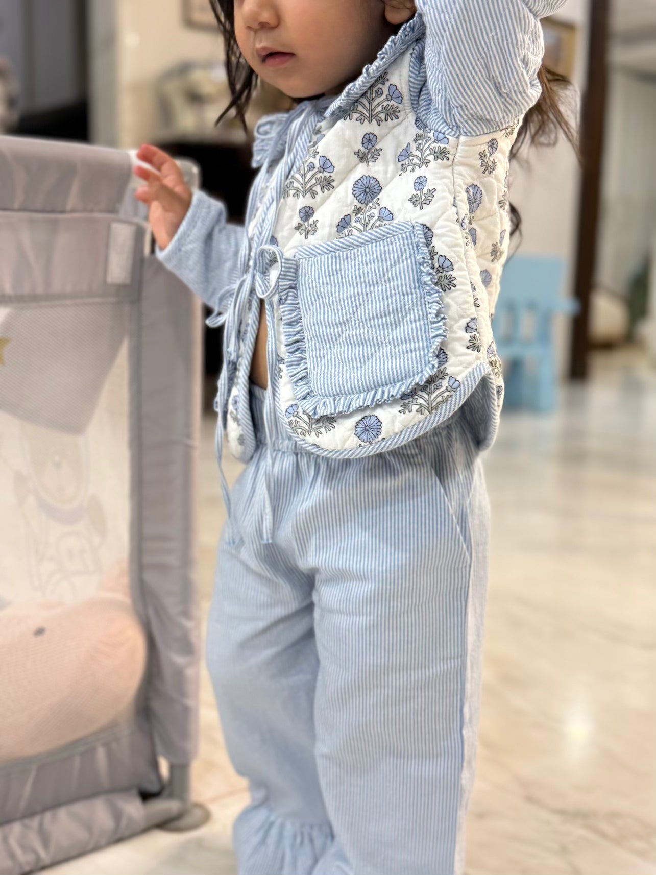 Child wearing a floral apron over a light blue outfit in an indoor setting