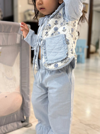 Child wearing a floral apron over a light blue outfit in an indoor setting