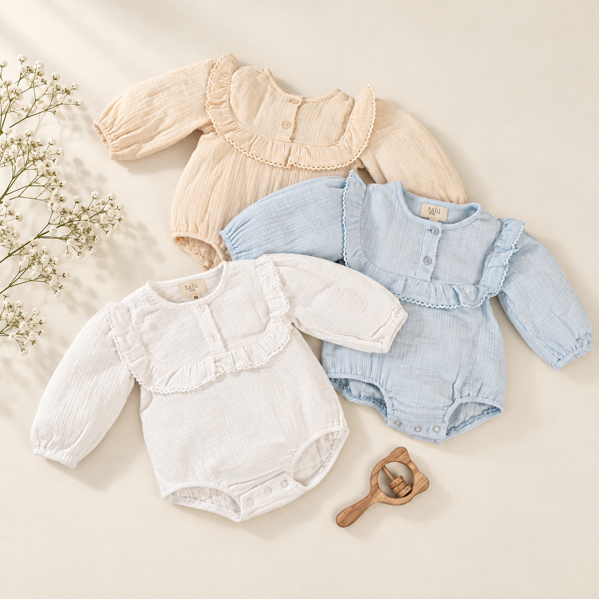 Three long-sleeve baby bodysuits with ruffled collars. The set includes cream, white, and light blue, beige.