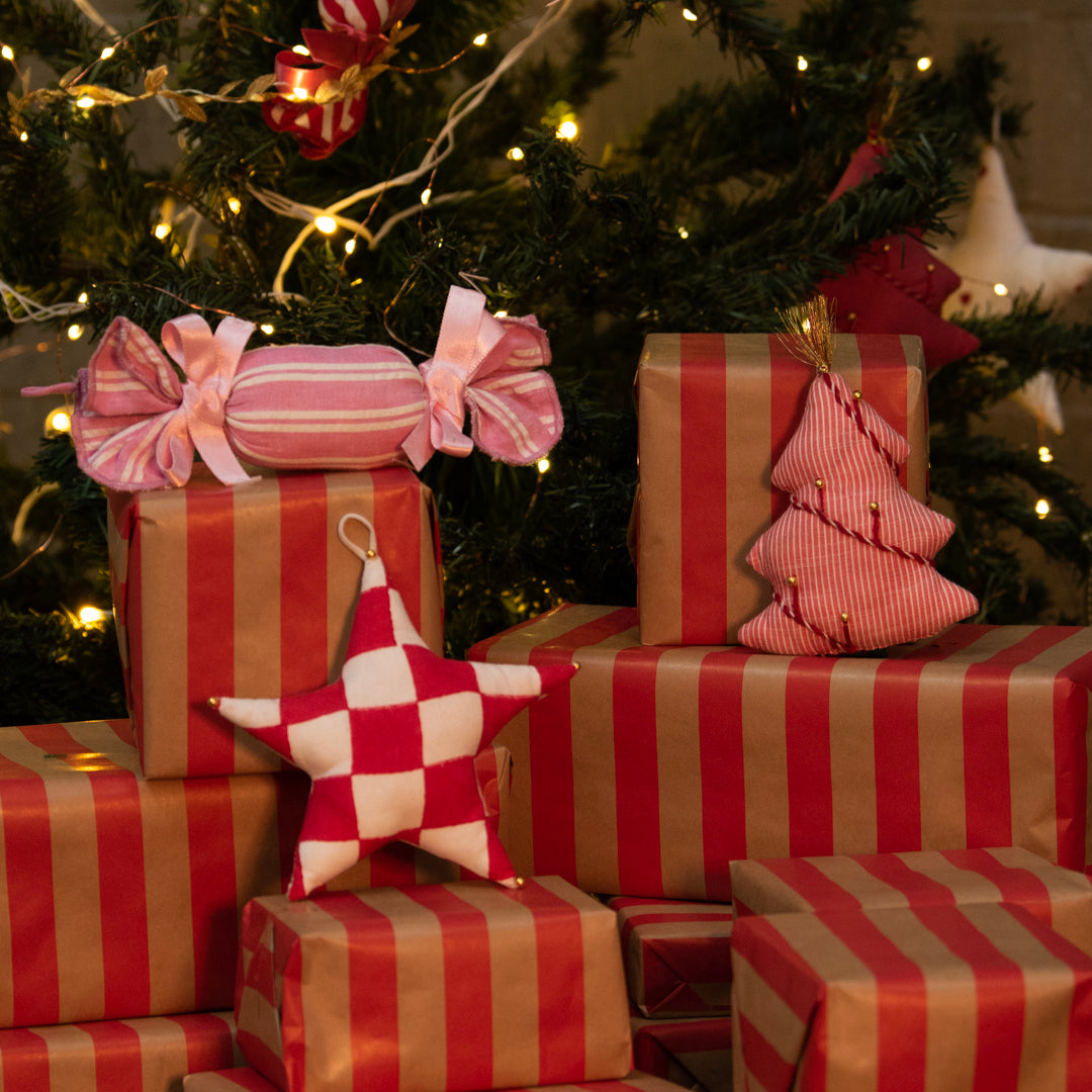 Stack of red and gold striped presents with decorative ribbons and stars in front of a Christmas tree.