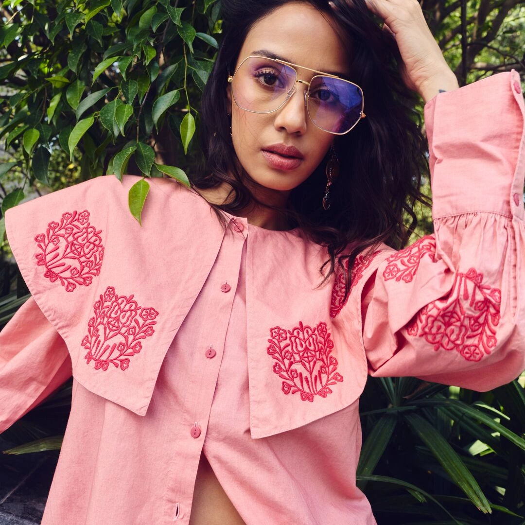 Woman wearing a pink embroidered blouse with a green leafy background